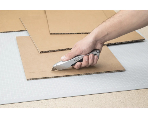 Main coupant du carton avec un cutter sur un tapis de découpe