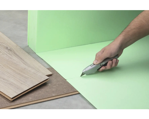 Une personne coupe une sous-couche isolante verte avec un cutter, à côté de laquelle se trouve du stratifié.