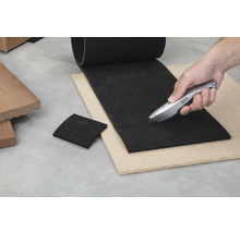 Découpe d'une sous-couche de terrasse noire avec un cutter sur une plaque de bois