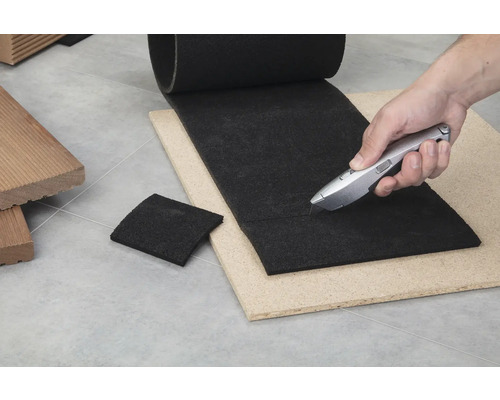 Découpe d'une sous-couche de terrasse noire avec un cutter sur une plaque de bois