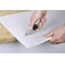 Personne coupant une plaque de plâtre avec un cutter