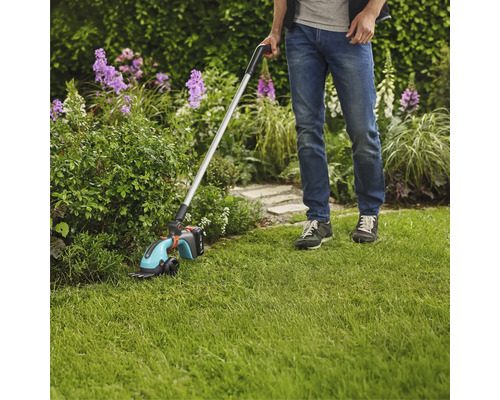 Homme utilisant une cisaille à gazon sans fil avec manche dans le jardin