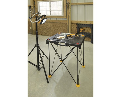 Werkstattsituation mit einer tragbaren Werkbank und einer Arbeitsleuchte auf einem Stativ.