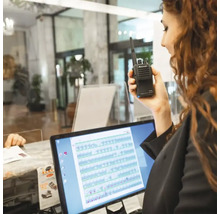 Frau hält ein Midland Funkgerät vor einem Computer.