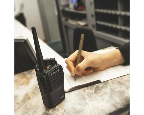 Ein Funkgerät der Marke Midland neben einer Person, die mit einem Stift auf Papier schreibt.