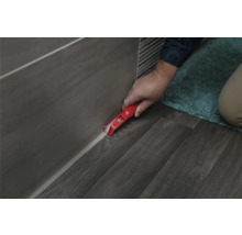 Un artisan retire des joints de silicone avec un grattoir à joints sur des carreaux et un sol.