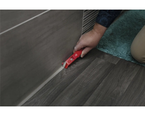 Un artisan retire des joints de silicone avec un grattoir à joints sur des carreaux et un sol.