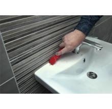 Une personne enlève du mastic d'étanchéité d'un lavabo avec un grattoir à joints