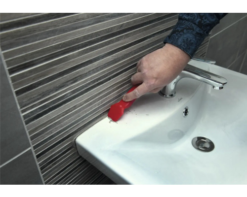 Une personne enlève du mastic d'étanchéité d'un lavabo avec un grattoir à joints