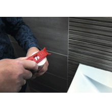 Une personne ouvre une cartouche avec un ouvre-cartouche rouge devant un mur carrelé.