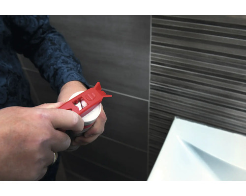 Une personne ouvre une cartouche avec un ouvre-cartouche rouge devant un mur carrelé.