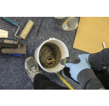 Mischen von Fliesenkleber im Eimer mit einem elektrischen Rührer. Werkzeuge und eine Person mit Schutzhandschuhen sind ebenfalls zu sehen.