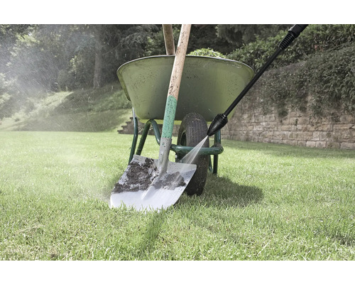 Nettoyage d'une pelle avec un nettoyeur haute pression à côté d'une brouette dans le jardin