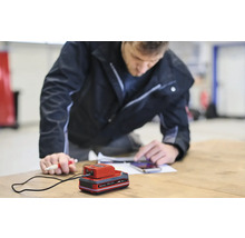 Ein Mann bedient ein Handy neben einem Ladegerät auf einem Tisch.