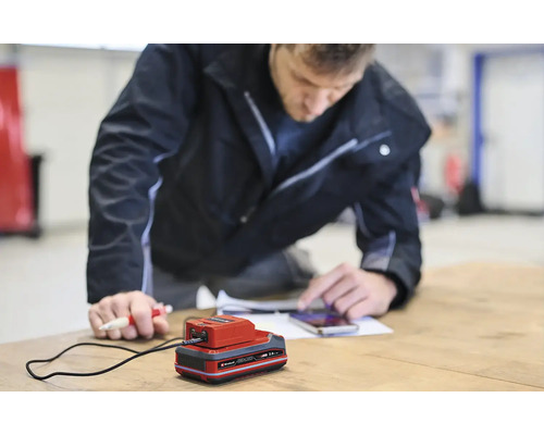 Ein Mann bedient ein Handy neben einem Ladegerät auf einem Tisch.