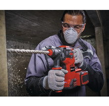 Mann bohrt mit einem Einhell Bohrhammer in eine Wand, wobei er Schutzbrille und Atemschutzmaske trägt