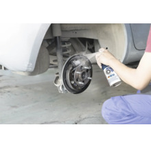 Eine Person reinigt eine offene Trommelbremse eines Autos mit Bremsenreiniger.