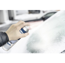 Une main tient un aérosol de dégivrant et pulvérise sur un pare-brise givré.