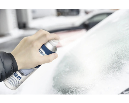 Une main tient un aérosol de dégivrant et pulvérise sur un pare-brise givré.