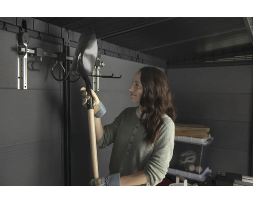 Femme tenant une pelle dans un abri de jardin avec système de suspension d'outils