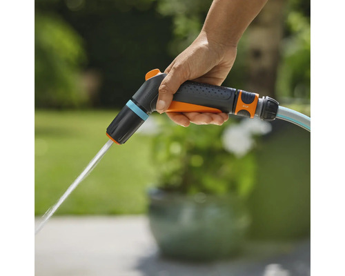 Une main tient un pulvérisateur de jardin Gardena d'où sort de l'eau.