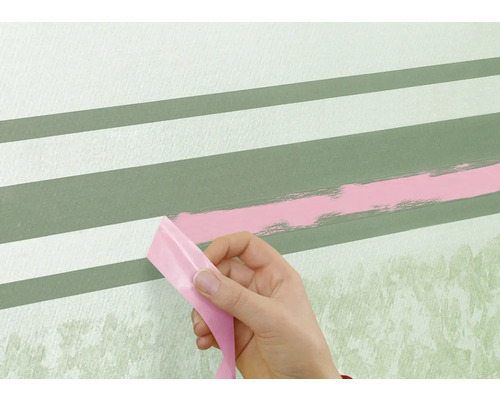 Une personne retire du ruban adhésif d'un mur avec des rayures peintes.