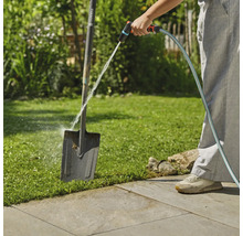 Scène de jardin avec une personne nettoyant une bêche avec un tuyau d'arrosage