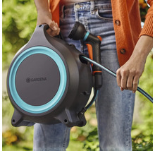 Une personne tient un dévidoir Gardena avec un tuyau d'arrosage et une lance.