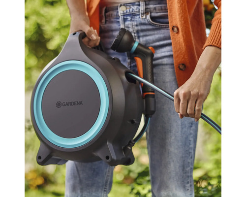 Une personne tient un dévidoir Gardena avec un tuyau d'arrosage et une lance.