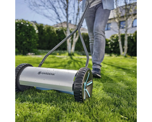 Tondeuse à gazon manuelle avec une personne dans le jardin.