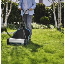 Une personne pousse une tondeuse à gazon manuelle Gardena sur une pelouse.