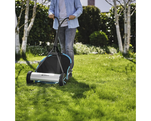 Une personne pousse une tondeuse à gazon manuelle Gardena sur une pelouse.