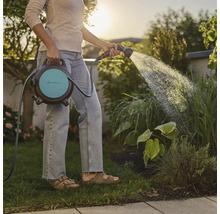 Une femme arrose le jardin avec un dévidoir Gardena