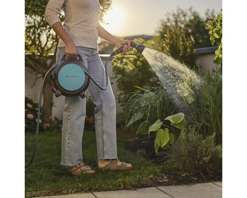Une femme arrose le jardin avec un dévidoir Gardena