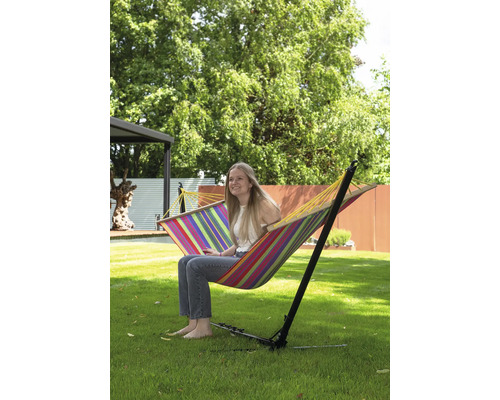 Femme assise dans un hamac rayé avec cadre dans le jardin.
