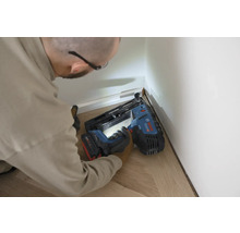 Artisan fixant des plinthes à un mur avec un cloueur à batterie