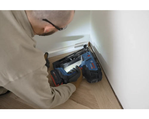 Artisan fixant des plinthes à un mur avec un cloueur à batterie