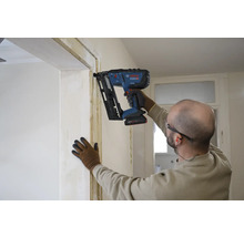 Un artisan fixe une latte sur un encadrement de porte à l'aide d'un cloueur à batterie.