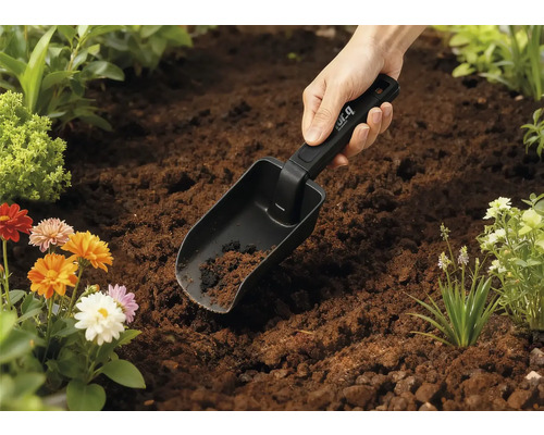 Gartenschaufel in der Erde mit Blumen im Hintergrund