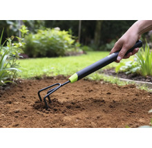 Gros plan d'une main enfonçant une griffe de jardin dans le sol