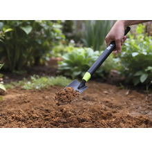 Une pelle à main avec de la terre est tenue devant un fond de jardin