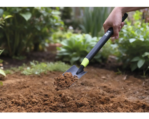 Une pelle à main avec de la terre est tenue devant un fond de jardin