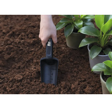 Une main tient une pelle à planter dans la terre, à côté de plantes en pot.