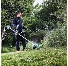 Un homme travaille avec un coupe-bordures à batterie dans le jardin pour couper l'herbe haute.