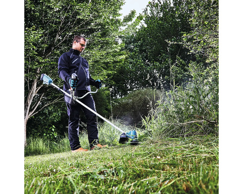 Un homme travaille avec un coupe-bordures à batterie dans le jardin pour couper l'herbe haute.