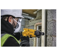 Un homme perce un trou dans un mur de briques avec une perceuse DeWalt.