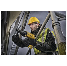 Un ouvrier perce un trou dans un mur avec une perceuse, debout sur un échafaudage.