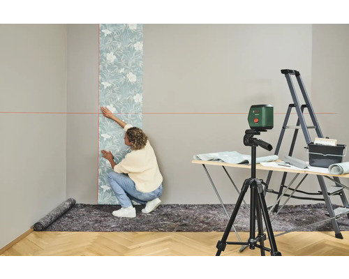 Femme tapissant un mur avec un niveau à bulle, une échelle et une table à tapisser