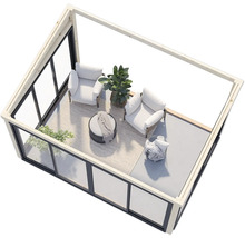 Innenraum mit Sesseln, Tisch und Pflanzen in einem Gartenhaus mit Glaswänden.