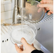 Une personne lave une cafetière à infusion froide sous un robinet.